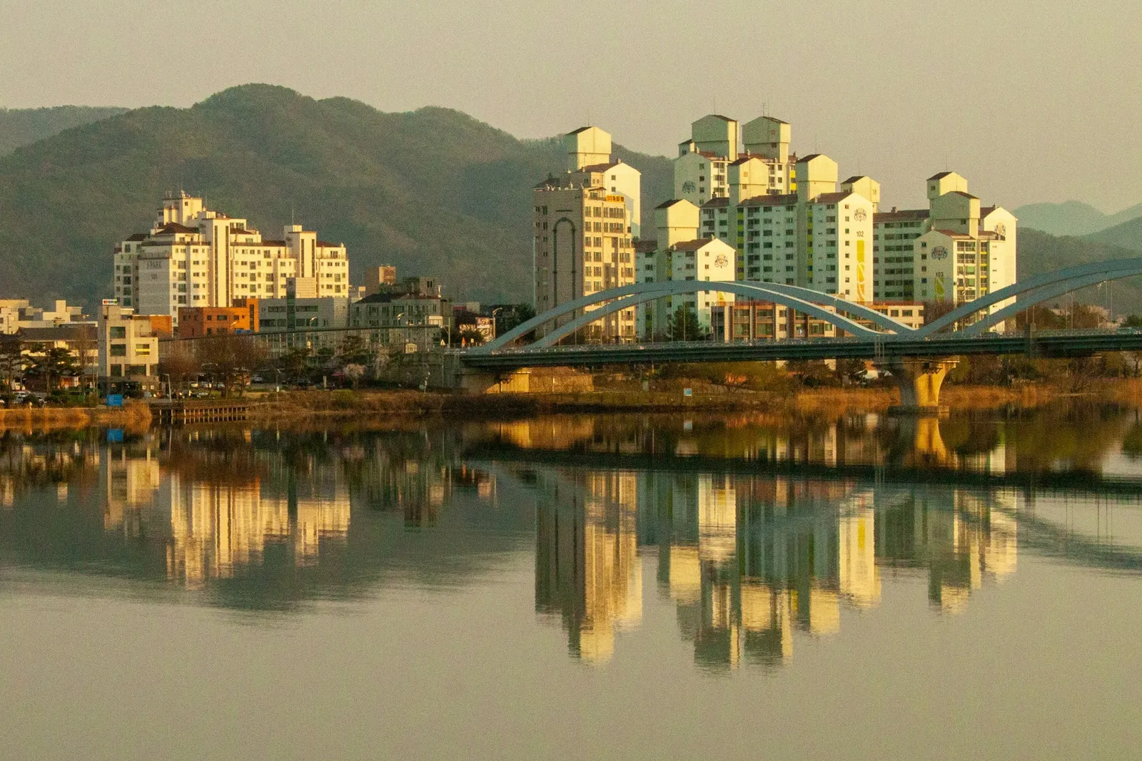 저녁 햇빛을 받은 강변 아파트와 아치 다리, 강물에 비친 반영