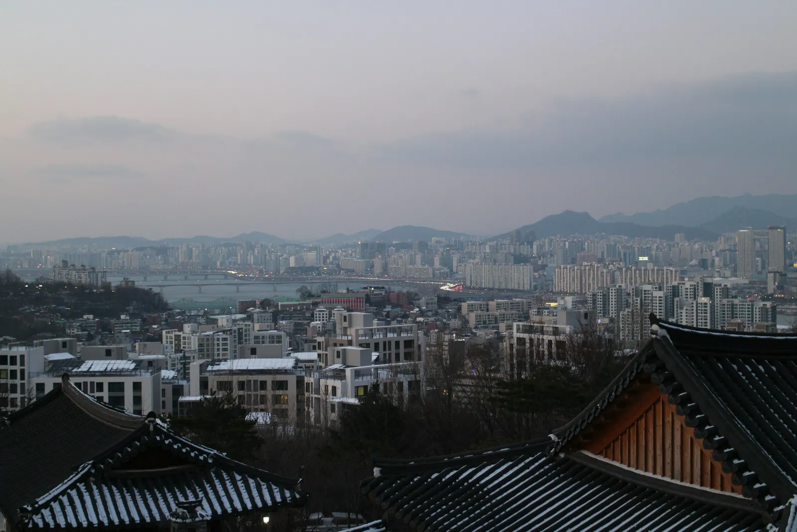 눈 쌓인 기와지붕 너머 겨울 저녁의 강과 강변 아파트