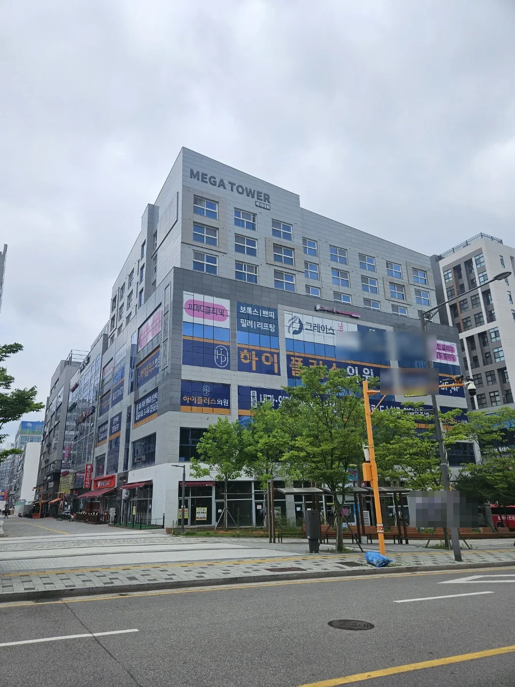 MEGA TOWER 간판이 걸린 상가 건물과 앞 보행로의 가로수